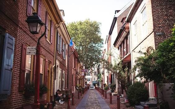 A brick-lined historic street in Philadelphia with cobblestones and greenery
