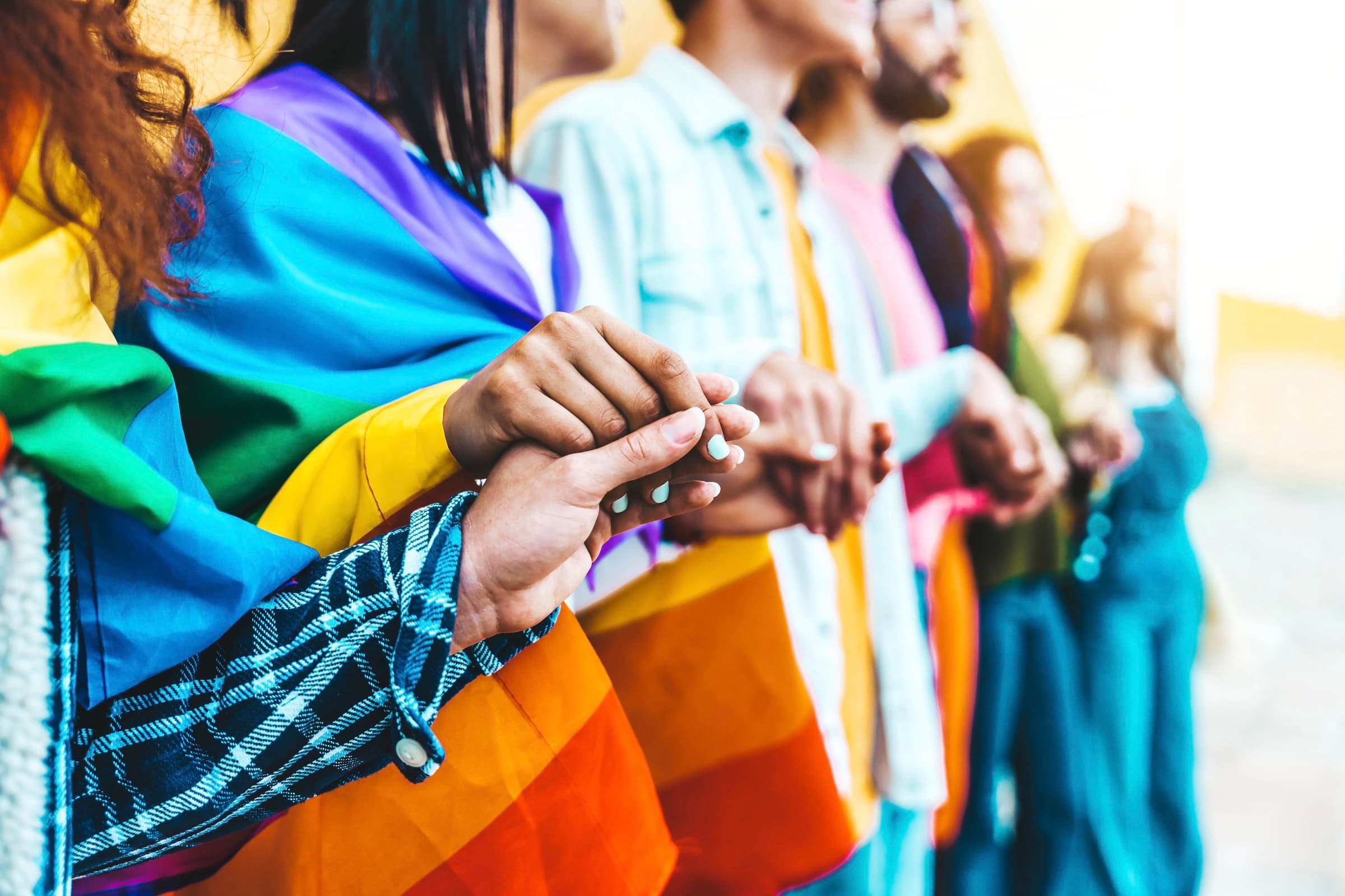 People holding hands, draped in rainbow pride flags